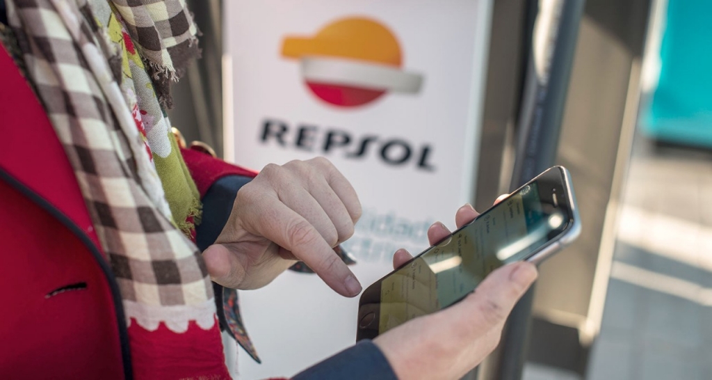 Persona utilizando el movil con cartel de Repsol de fondo